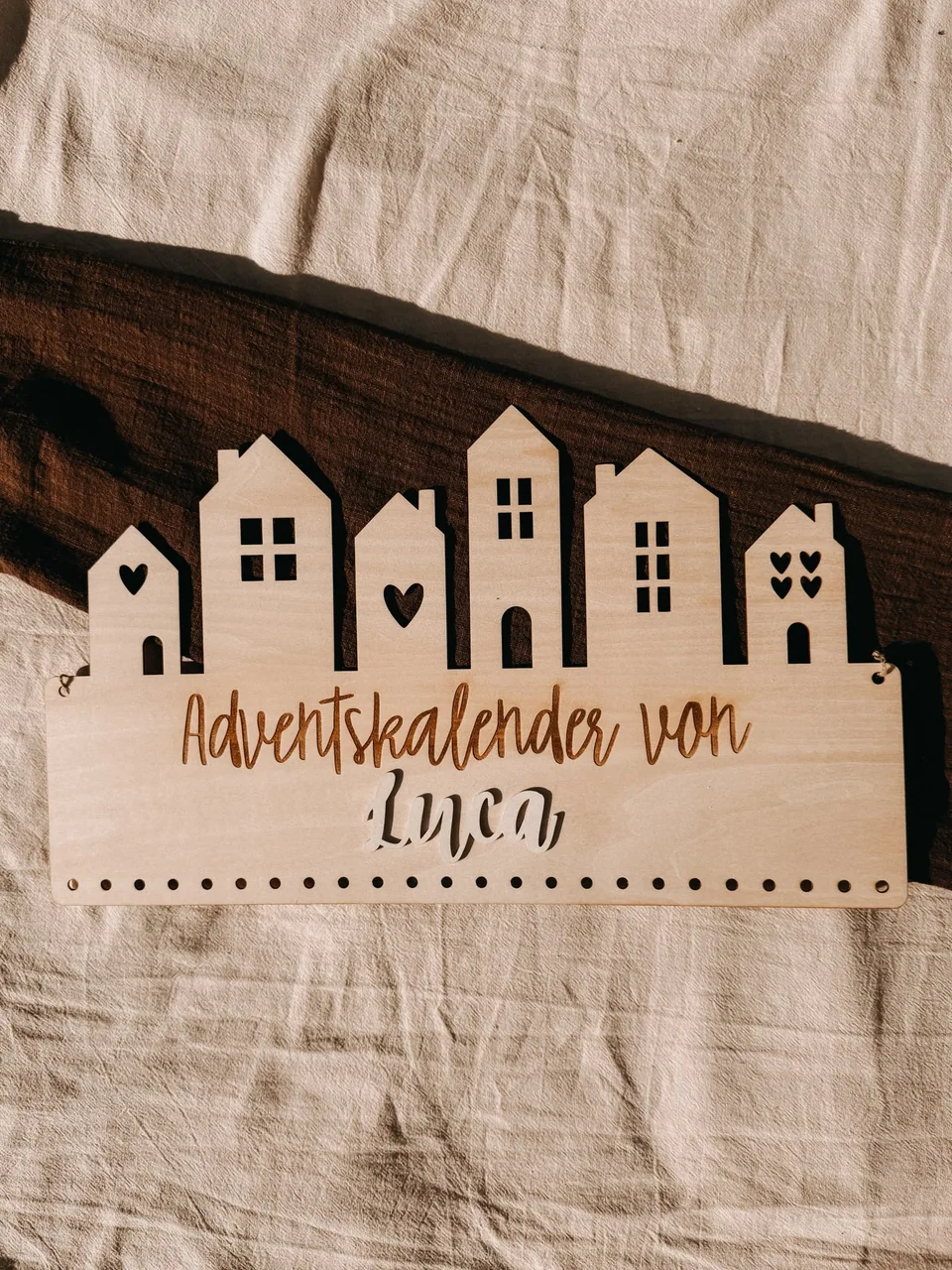 Hölzerner Adventskalender mit Häusersilhouetten, dem Namen Luca und Löchern zum Aufhängen kleiner Geschenke