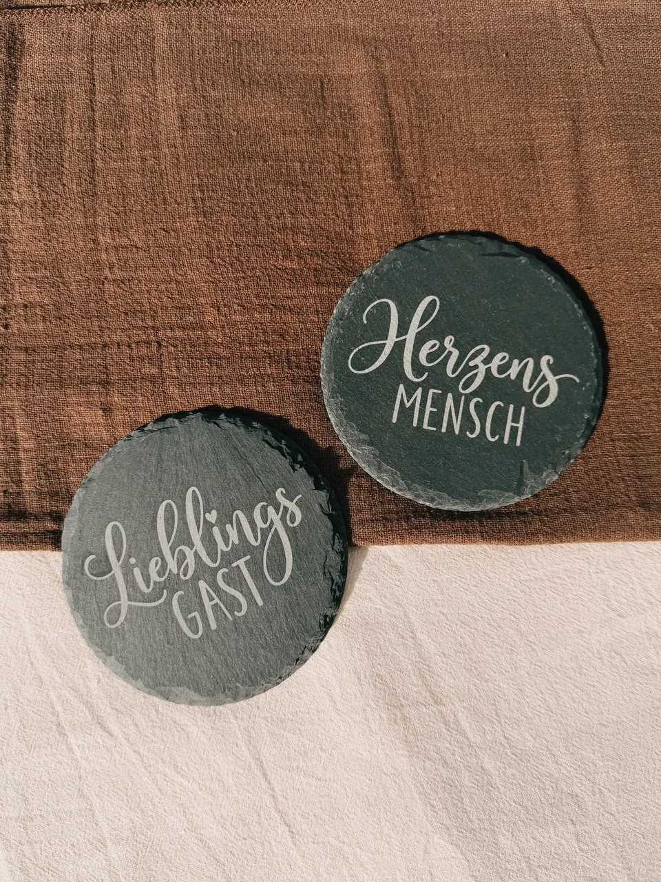 Zwei runde Schieferuntersetzer mit den Gravuren „Lieblingsgast“ und „Herzensmensch“